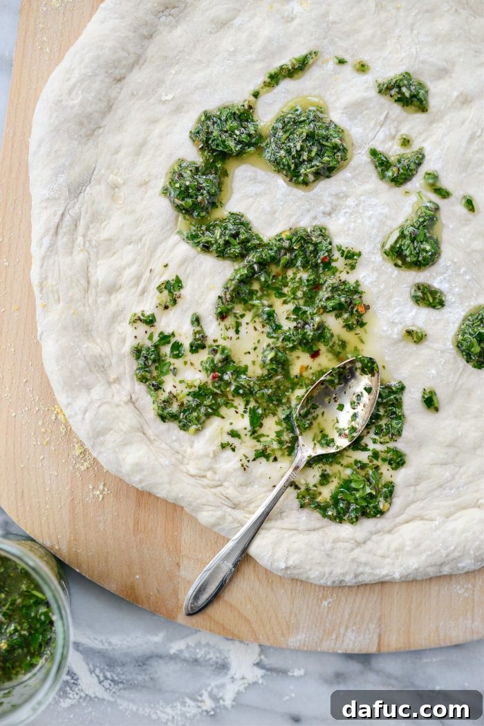 Homemade chimichurri sauce being spread onto pizza dough