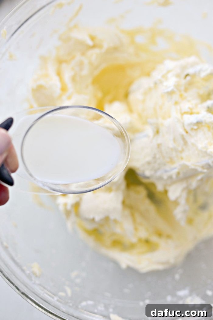 Tangy Lemon Cupcakes with Velvety Frosting 14 Milk being poured into the buttercream mixture in a mixing bowl
