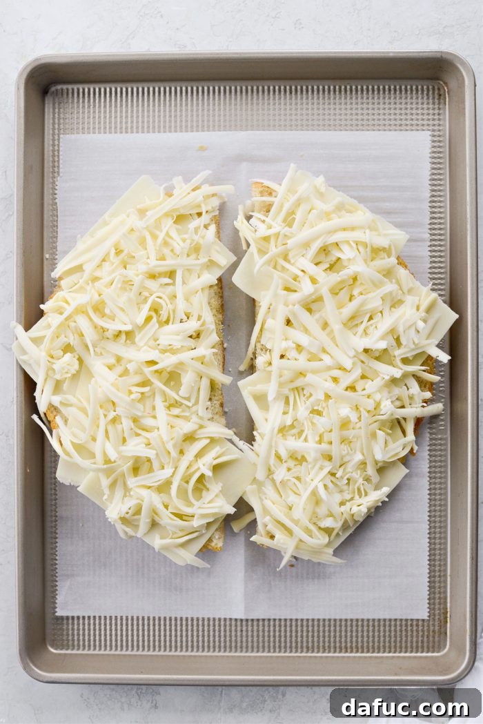 Old World Italian Sub 6 Focaccia halves topped generously with slices of mozzarella and grated fontina cheese, ready for the oven.