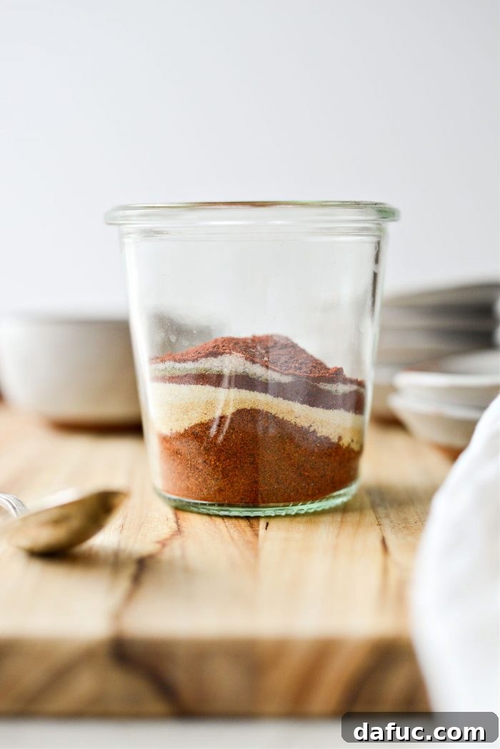 Hands carefully measuring various spices into a glass jar, demonstrating the blending process for street taco seasoning.