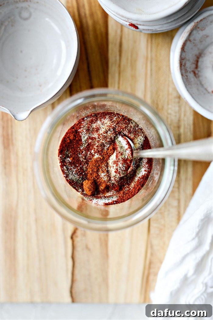 A hand whisking chili powder, paprika, garlic powder, and other spices together in a bowl until fully combined.