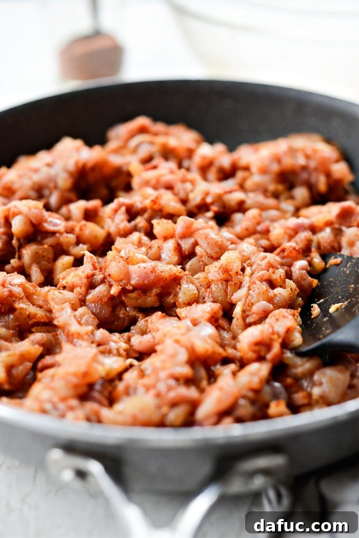 Adding seasoned minced chicken to a hot skillet, spreading it into an even layer