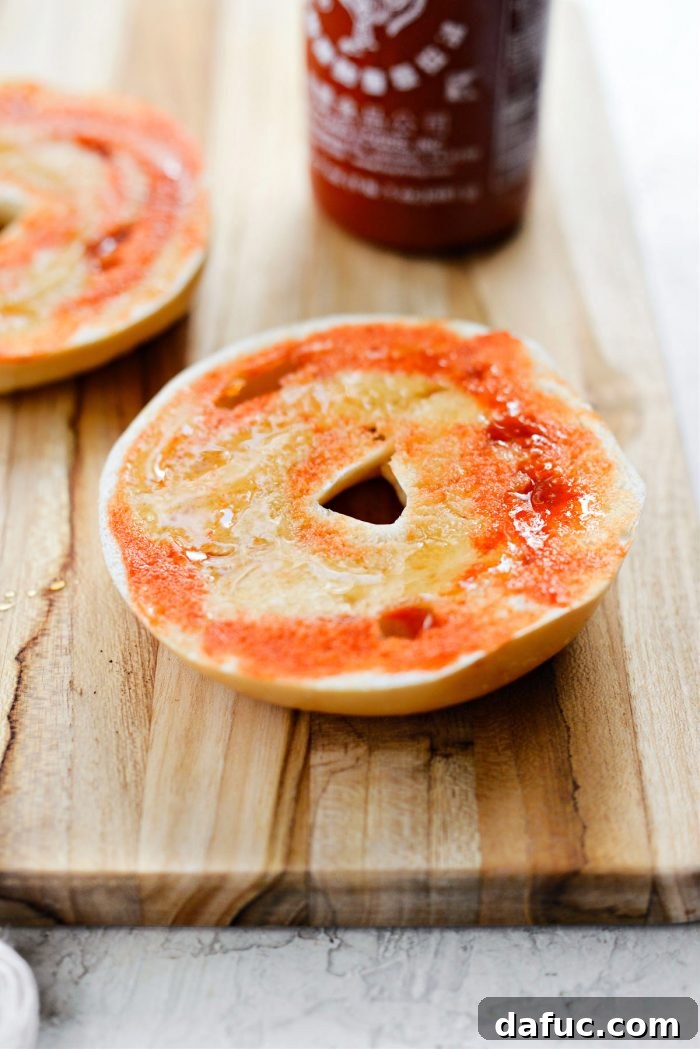 Sweet & Spicy Bagel with Zesty Chive Cream Cheese 10 A knife spreading honey and sriracha evenly over a bagel half