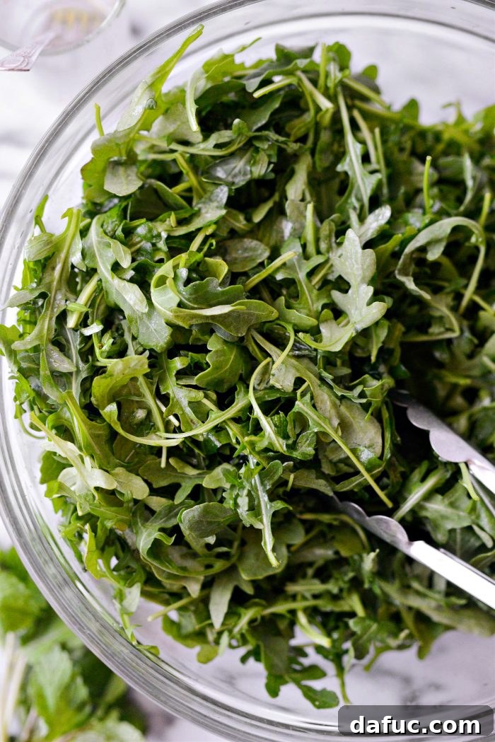 Summer Berry Caprese Salad 8 Arugula being tossed gently with dressing using tongs