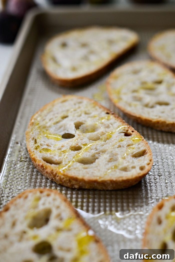 Slices of crusty bread drizzled with olive oil on a baking sheet, ready for toasting