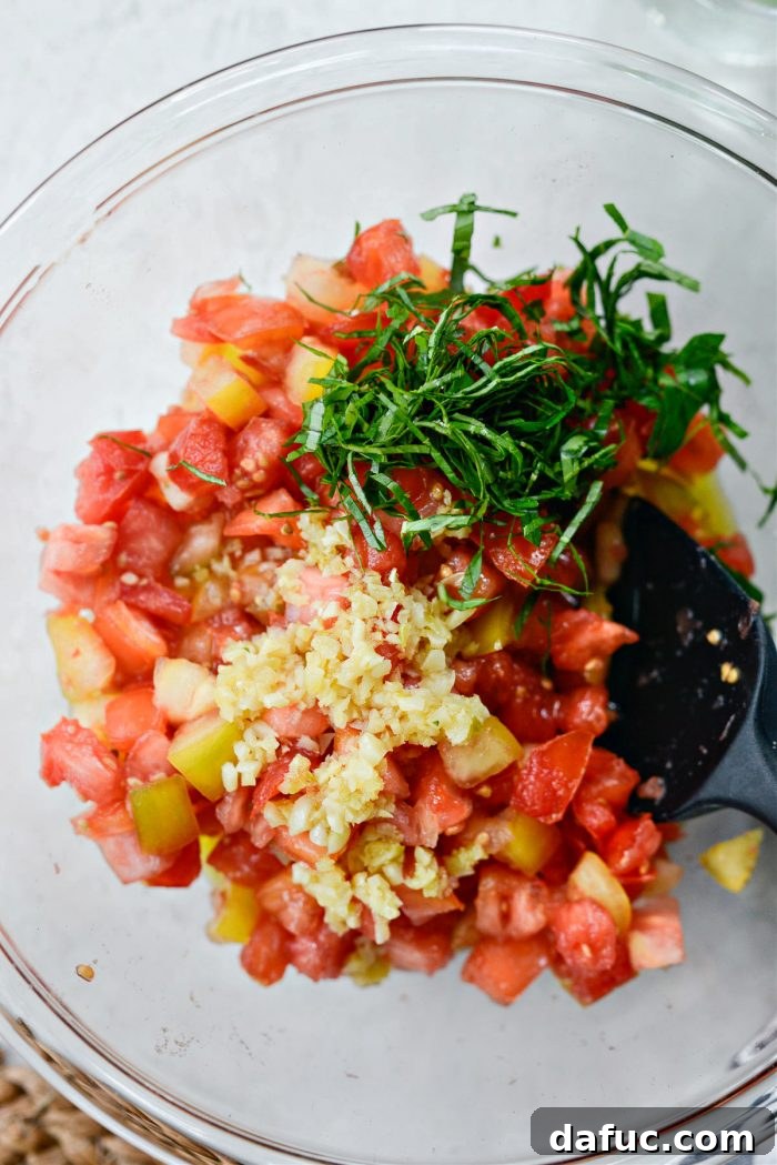 Vibrant Heirloom Tomato Bruschetta 15 Garlic oil and thinly sliced basil being added to the bowl of drained heirloom tomatoes.