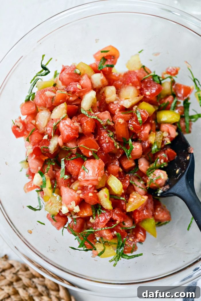 Vibrant Heirloom Tomato Bruschetta 16 The heirloom tomato, garlic oil, and basil mixture being gently tossed in a bowl to combine all ingredients.