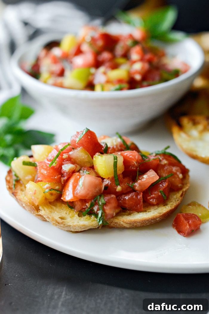 Vibrant Heirloom Tomato Bruschetta 3 Two vibrant, perfectly ripened heirloom tomatoes sitting beside fresh basil and garlic, showcasing the primary ingredients for bruschetta.