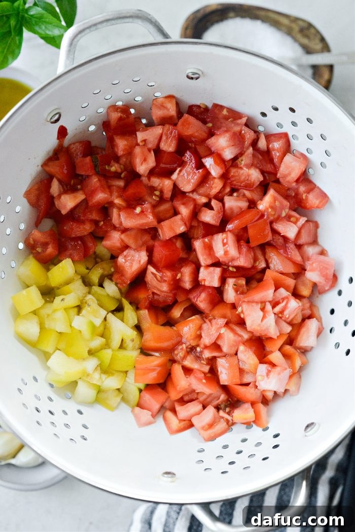 Vibrant Heirloom Tomato Bruschetta 5 A white colander filled with small, uniformly diced heirloom tomatoes, positioned over a collecting bowl.
