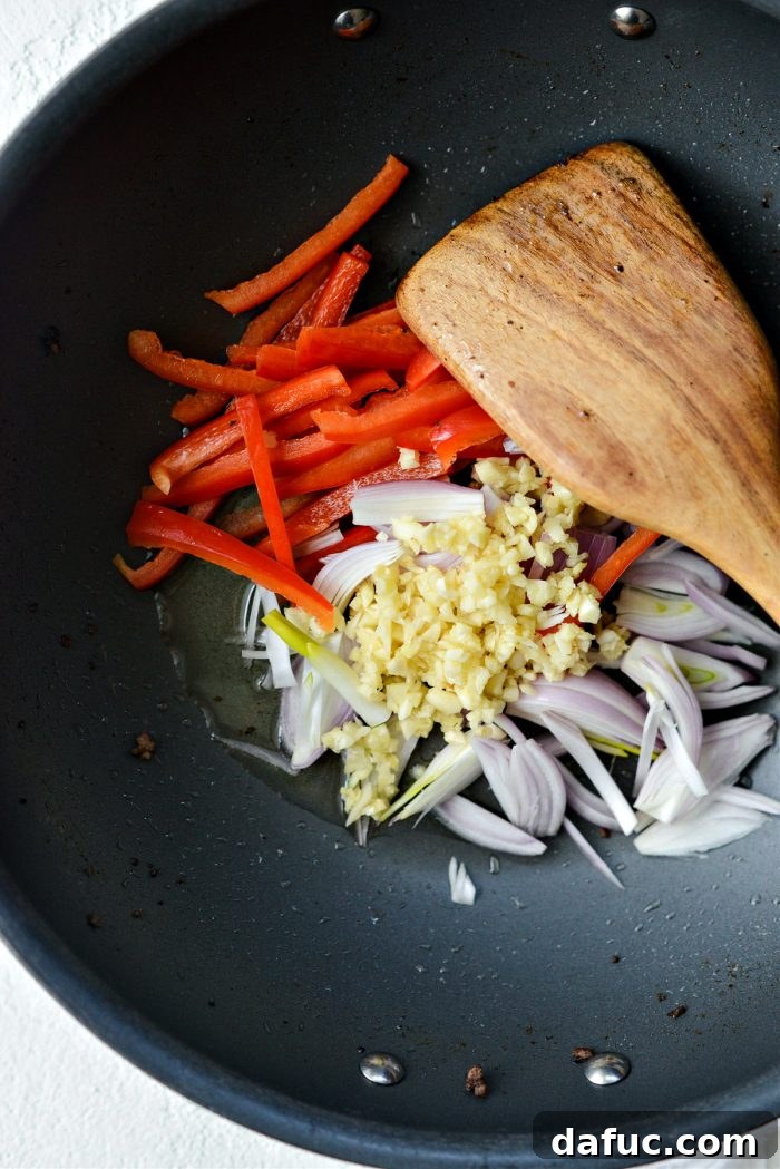 Sliced bell peppers, shallots, and minced garlic added to a pan