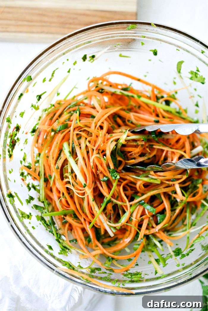 Vibrant Thai Carrot Slaw 8 Hands tossing the Thai Carrot Slaw with tongs, ensuring all ingredients are coated.