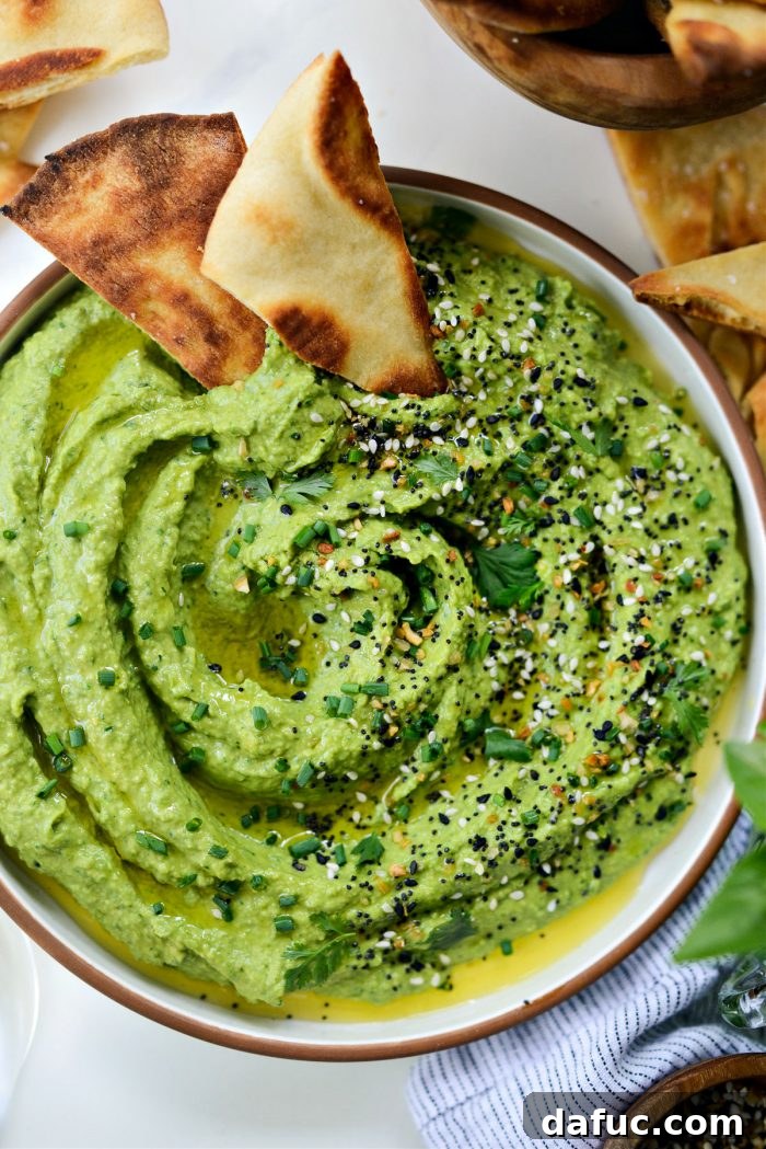 Vibrant Green Goddess Hummus 12 A bowl of Green Goddess Hummus on a wooden board with various dipping vegetables and pita bread
