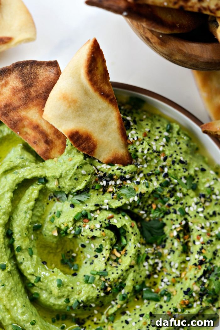 Vibrant Green Goddess Hummus 13 Overhead shot of Green Goddess Hummus with a spoon, fresh herbs, and pita triangles