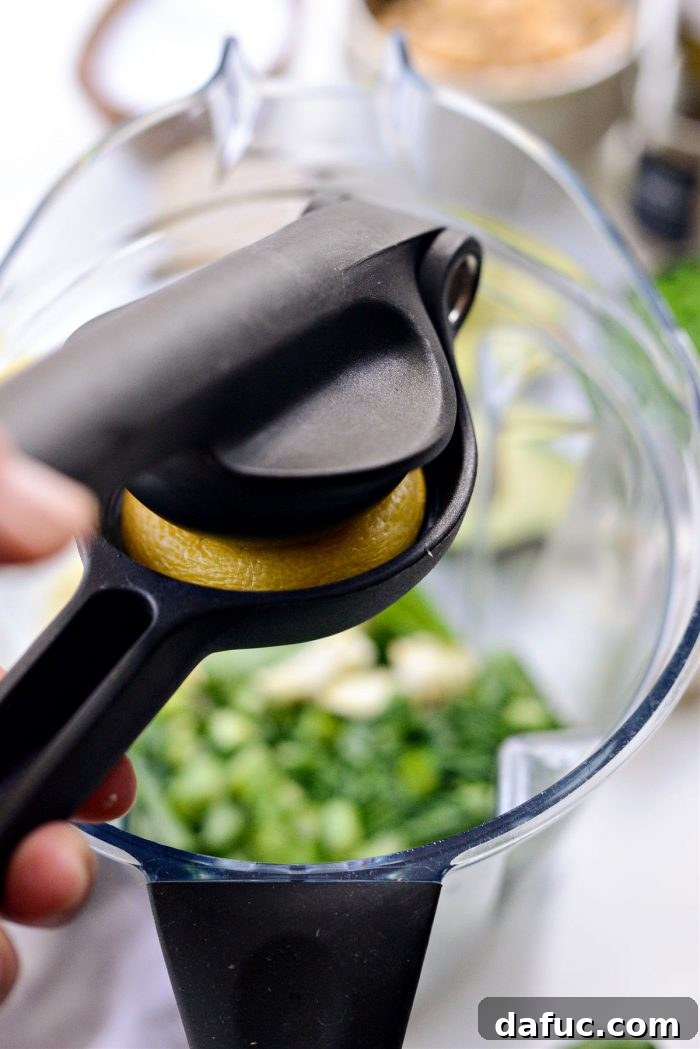Vibrant Green Goddess Hummus 6 Hand squeezing fresh lemon juice into a blender with herbs and garlic