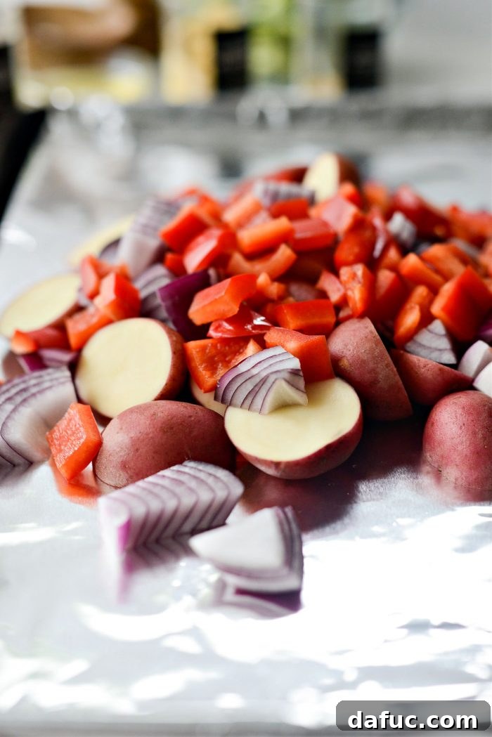 Potatoes, onions, and peppers on a lined sheet pan before roasting
