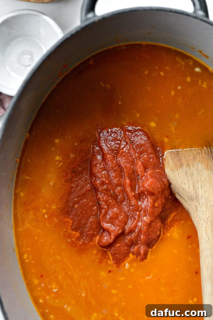 Adding crushed tomatoes to the soup base.