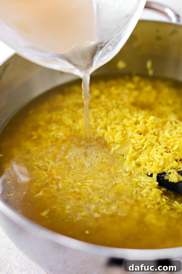 Golden Turmeric Rice 12 Pouring chicken broth into the pot with rice