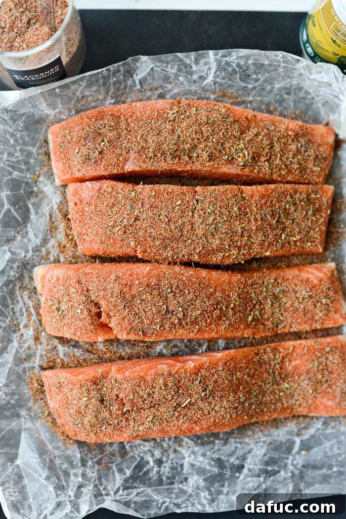 Applying a generous amount of blackened seasoning to the top of a salmon fillet