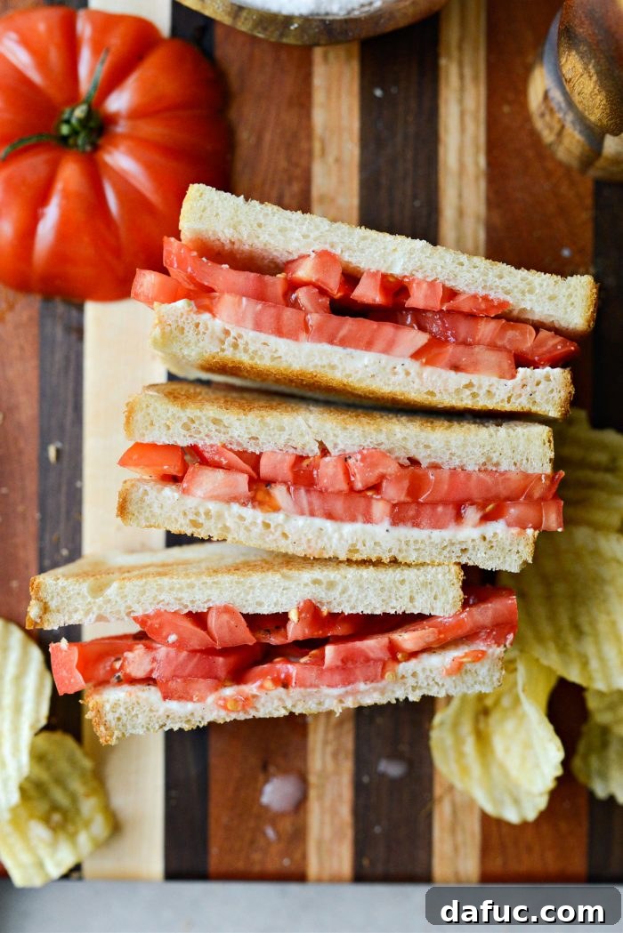 A close-up of a Classic Tomato Sandwich with potato chips and iced tea, showcasing the ideal summer meal.
