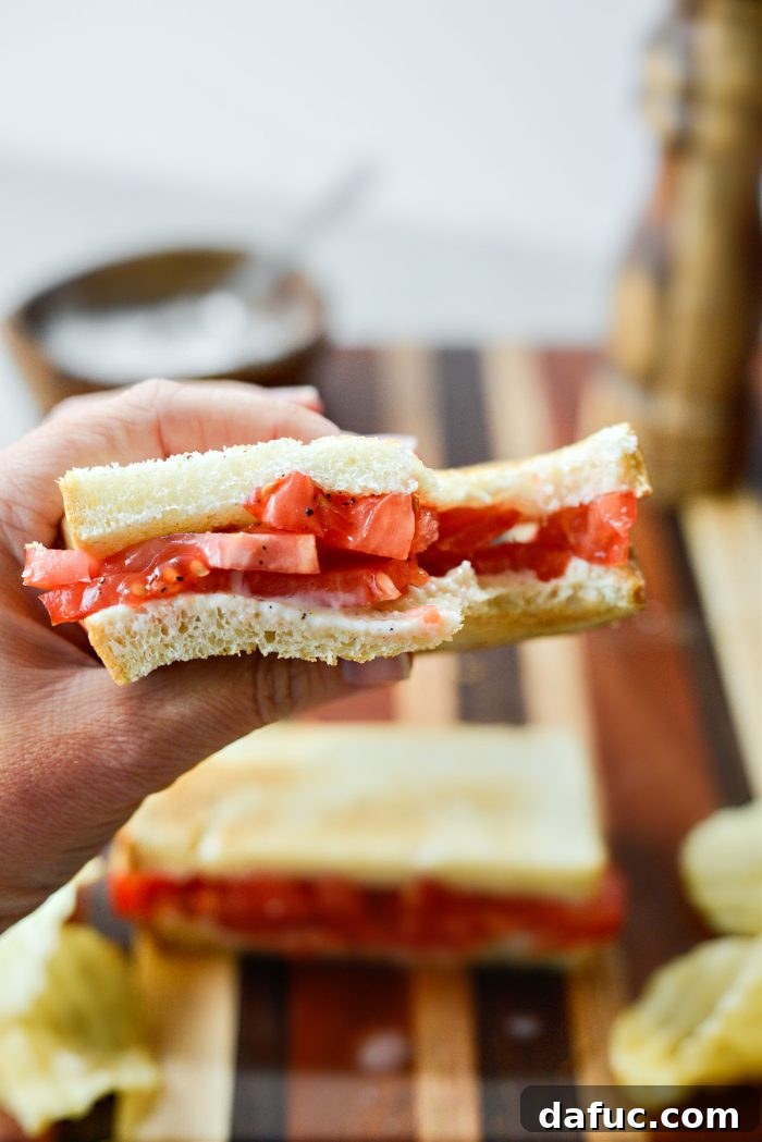 A delicious bite taken out of a Classic Tomato Sandwich, revealing the juicy layers.
