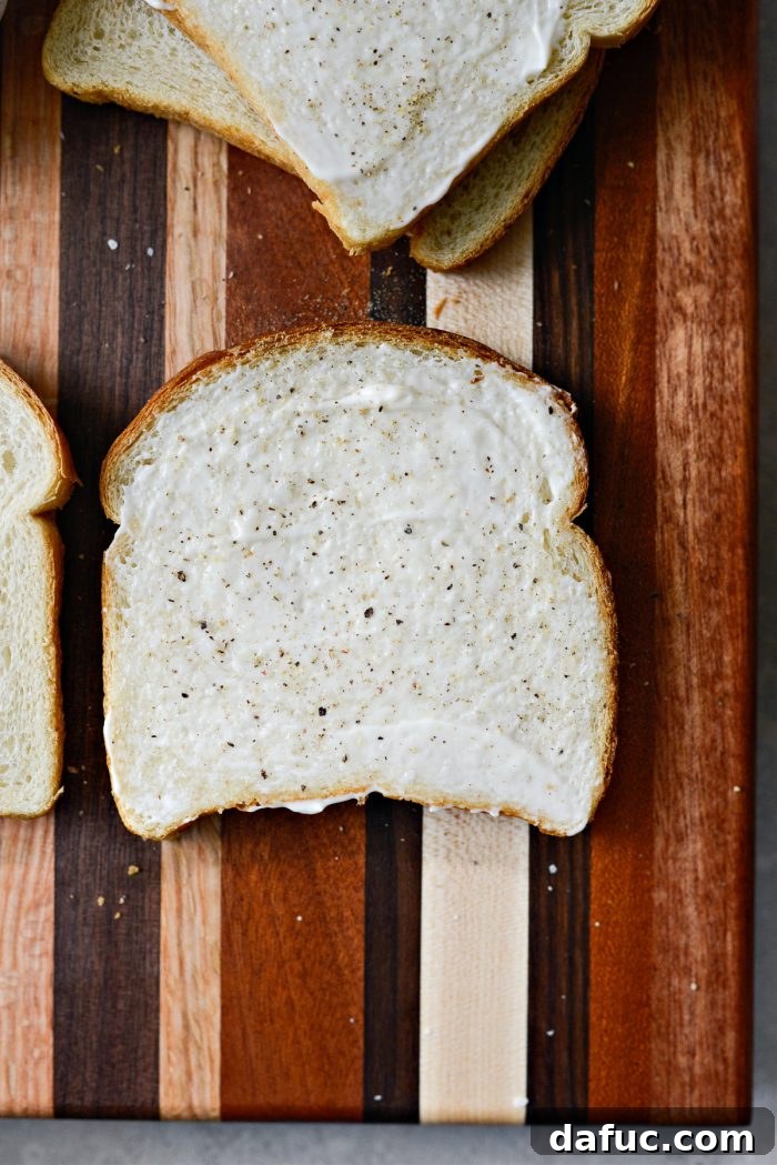 A slice of bread spread with a thin layer of mayonnaise, seasoned with kosher salt and freshly ground black pepper.