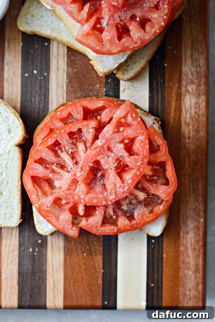 Freshly sliced tomatoes arranged on mayonnaise-coated bread, generously seasoned with salt and pepper.
