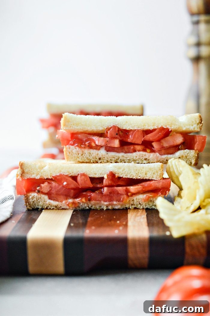 A side view of a sliced Classic Tomato Sandwich, showing the distinct layers of bread, mayonnaise, and thick-cut tomatoes.