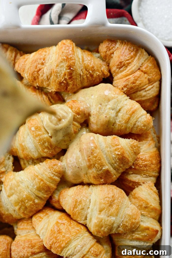 The remaining eggnog custard being poured evenly over the top layer of croissants.