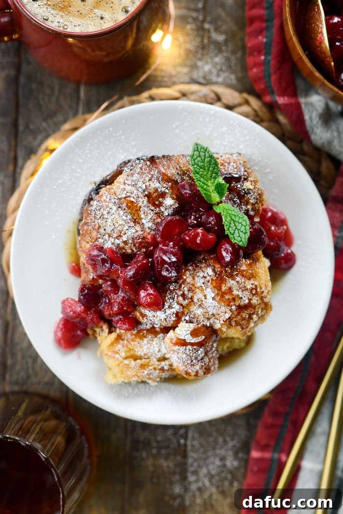 A close-up shot of the baked Eggnog Croissant French Toast Bake, showing its golden crust and fluffy texture, ready for serving with cranberry relish and maple syrup.