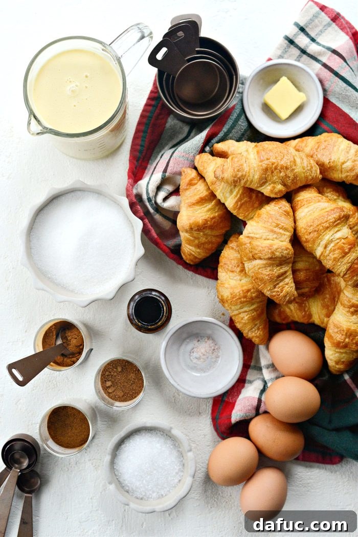 Ingredients for Eggnog Croissant French Toast Bake laid out on a table, including croissants, eggnog, eggs, spices, and cranberries.