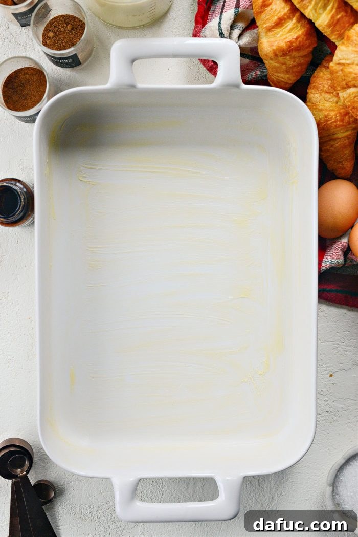 A 9x13 baking dish being greased with butter, preparing for the Eggnog Croissant French Toast Bake.