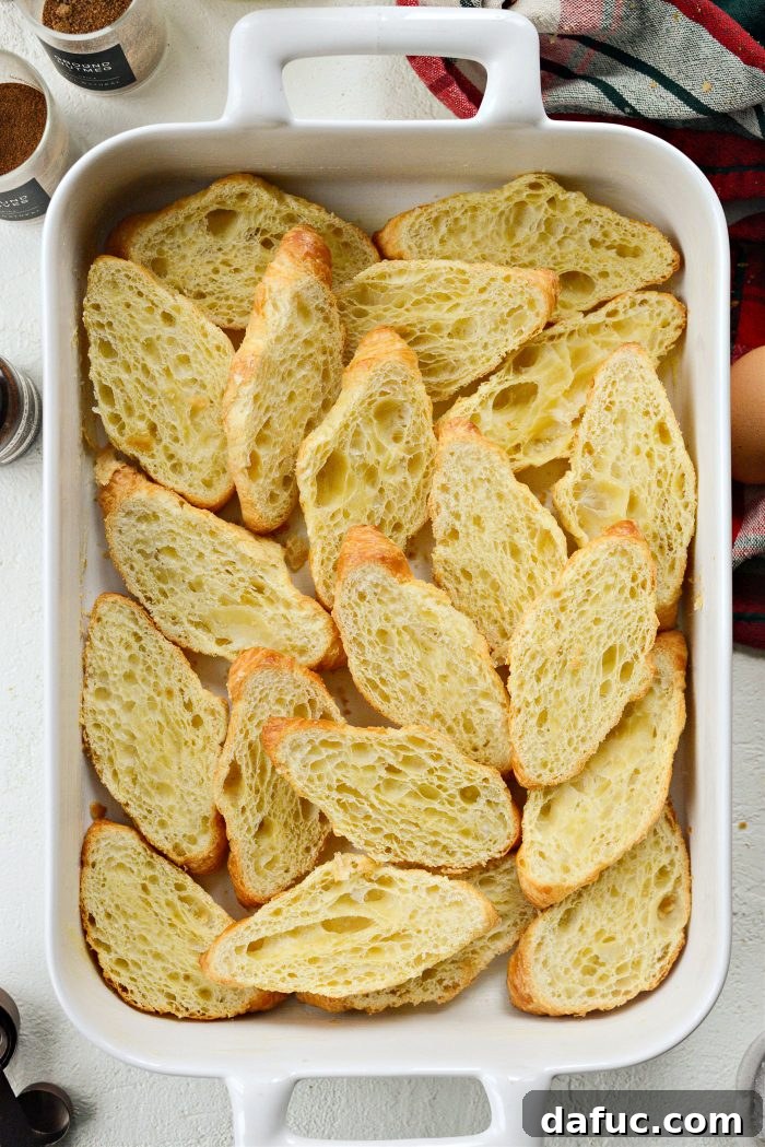 The bottom halves of croissants arranged neatly in a greased 9x13 baking dish, forming the base for the French toast bake.