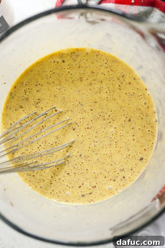 A whisk thoroughly combining the eggnog custard ingredients in a mixing bowl.