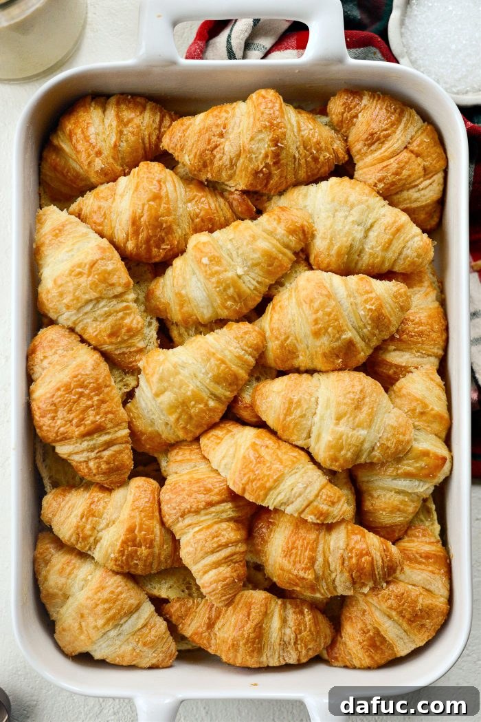 The top halves of the croissants being arranged over the custard-soaked bottom halves in the baking dish.
