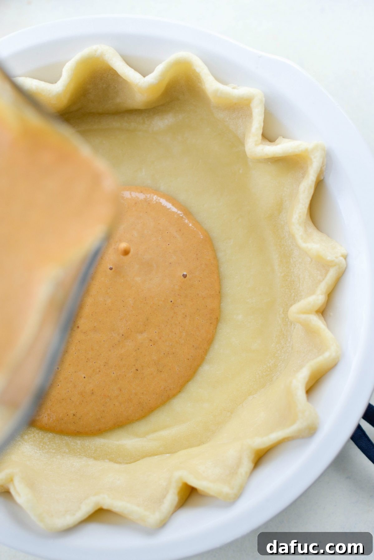 Pouring creamy pumpkin pie filling into a partially baked pie crust
