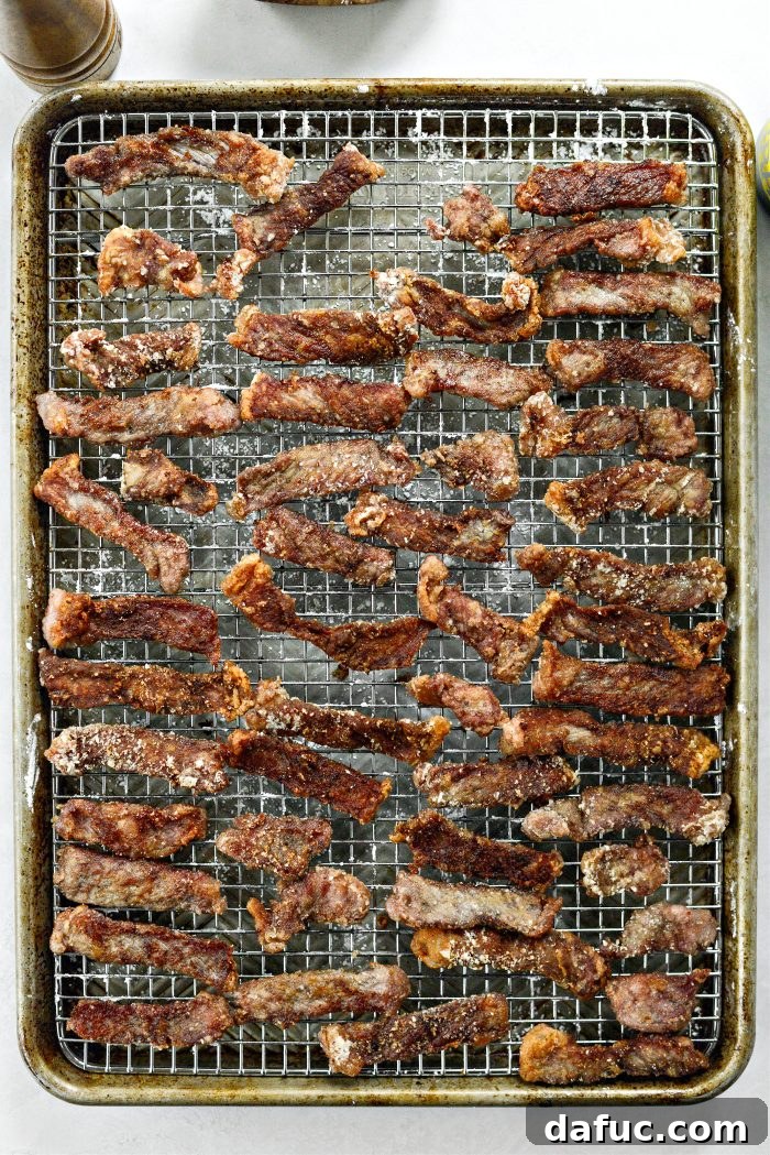 Cooked crispy beef strips gracefully transferred back to the wire rack, allowing excess oil to drain.