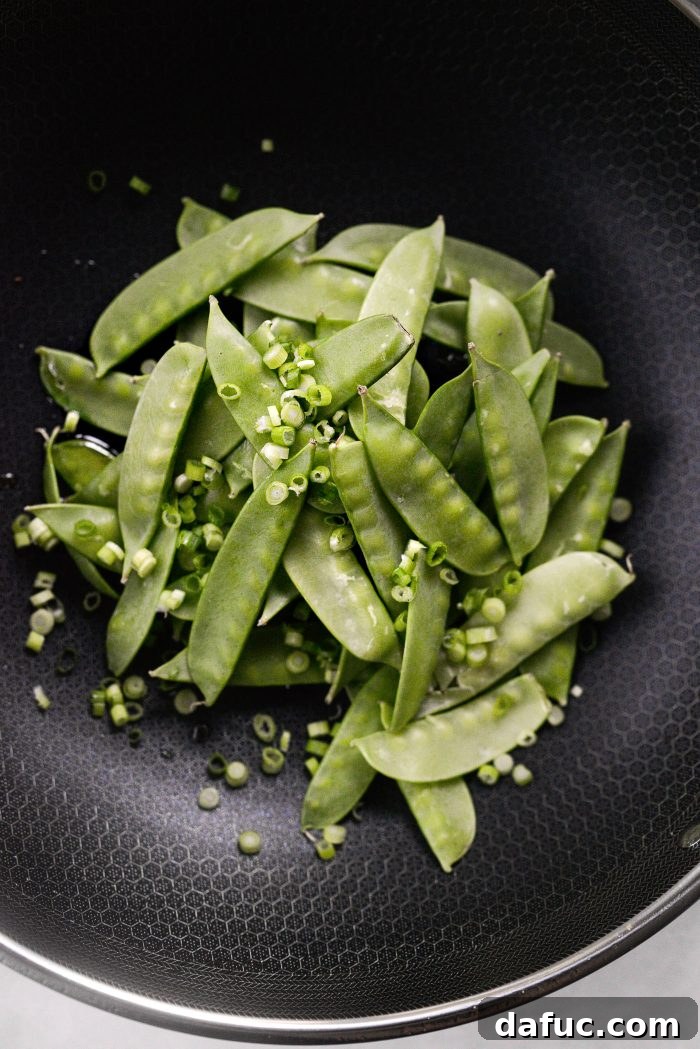 Spicy-Sweet Crispy Beef and Snap Peas 16 Vibrant snow peas and sliced green onions being expertly stir-fried in a skillet with fragrant sesame oil.