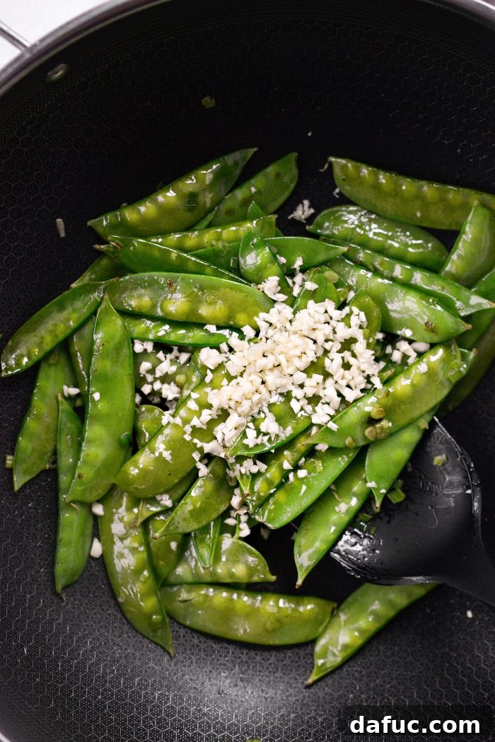 Spicy-Sweet Crispy Beef and Snap Peas 17 Freshly minced garlic being added to the stir-frying snow peas and green onions in the skillet.