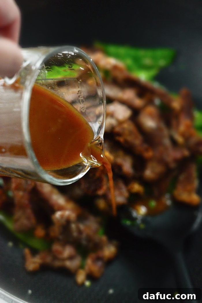 Spicy-Sweet Crispy Beef and Snap Peas 19 The vibrant honey sriracha sauce being generously poured over the crispy beef and vegetables in the skillet.