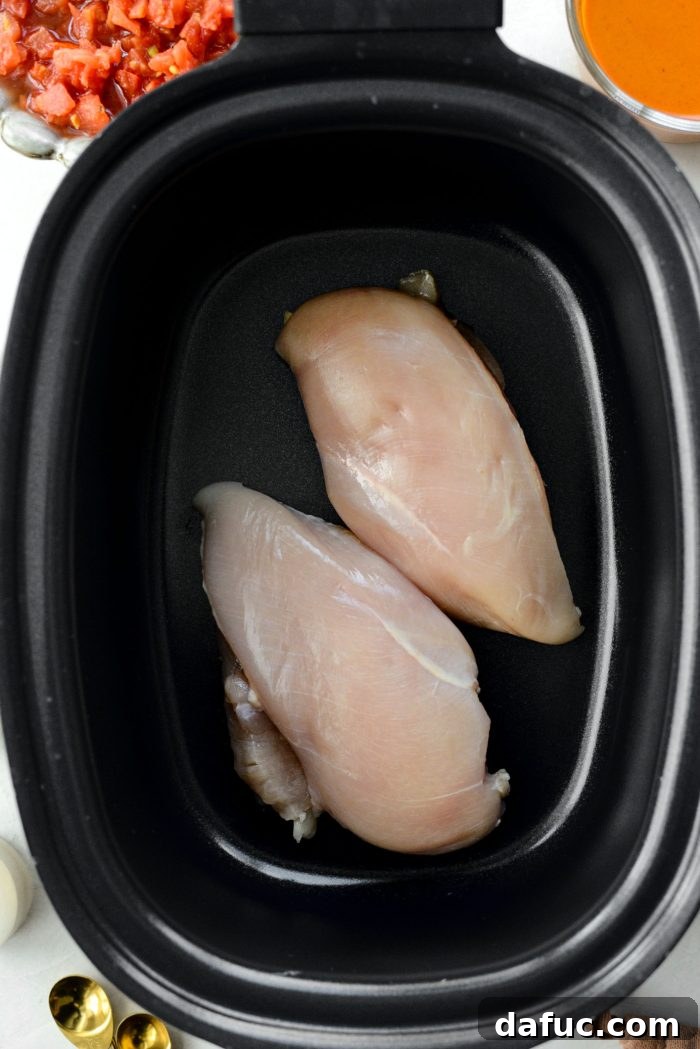 Adding chicken breasts to the slow cooker for buffalo chicken chili