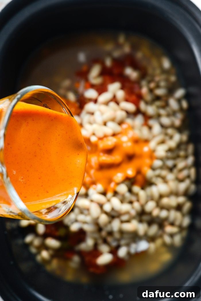 Pouring buffalo sauce into the slow cooker chili