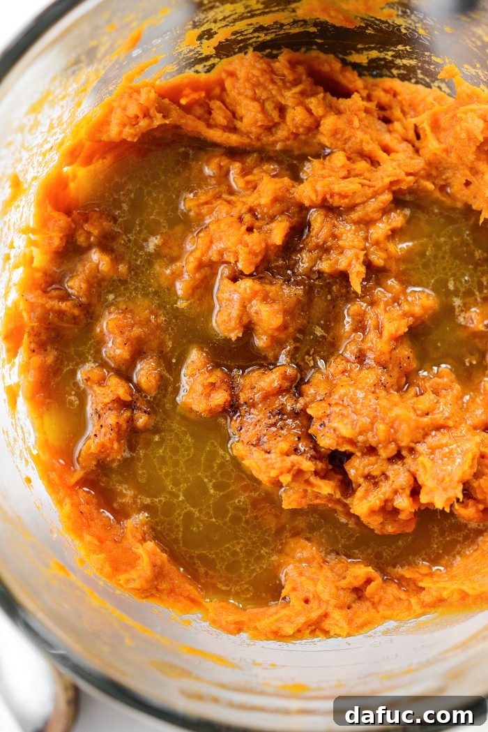 Pouring bourbon butter mixture into sweet potatoes in a mixer