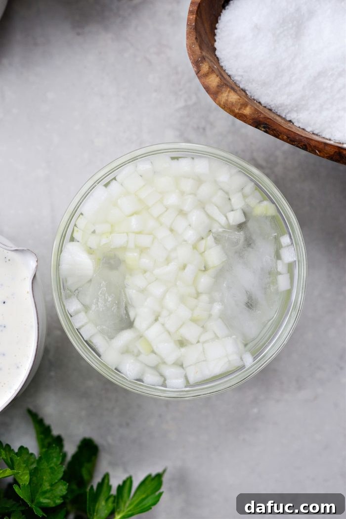 Finely diced yellow onions soaking in a bowl of ice water, a key step for mellowing their flavor.