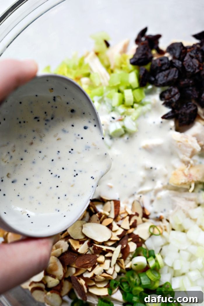 Pouring the creamy dressing over the prepped salad ingredients in a mixing bowl.