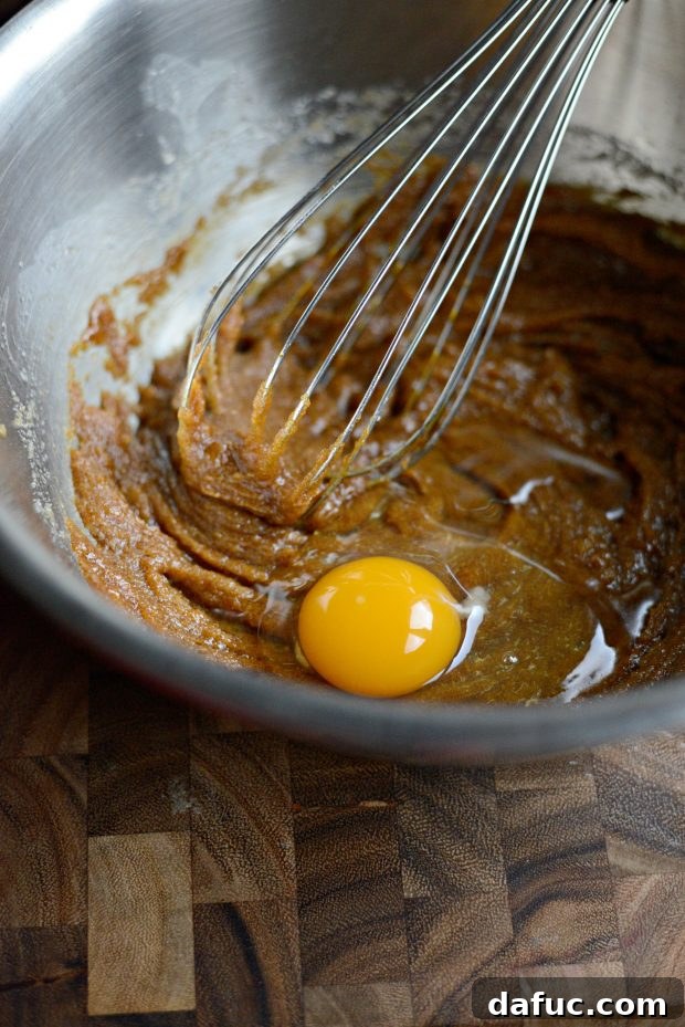 Golden Molasses Chews 8 Adding and whisking an egg into the wet molasses cookie mixture.