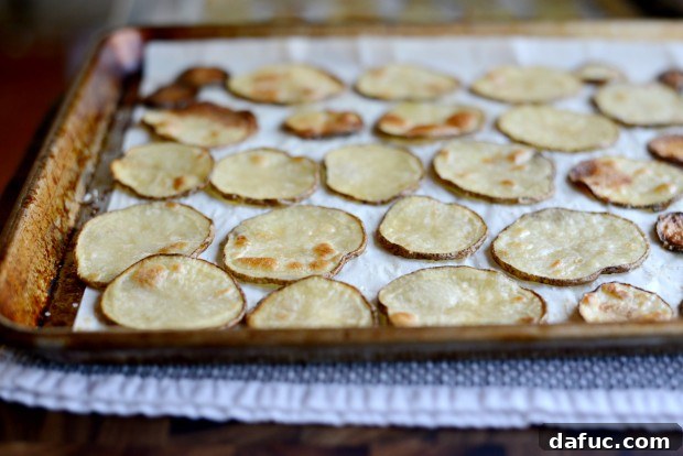 Oiled and seasoned potato slices arranged in a single layer on a parchment-lined baking sheet, prepared for oven baking.
