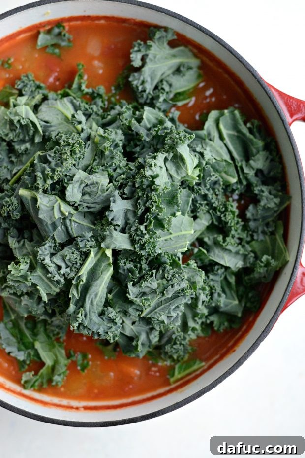 Chopped kale being stirred into the simmering minestrone soup.