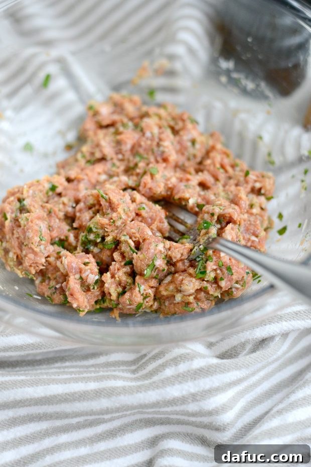 A fork mixing the turkey meatball ingredients in a bowl until just combined.