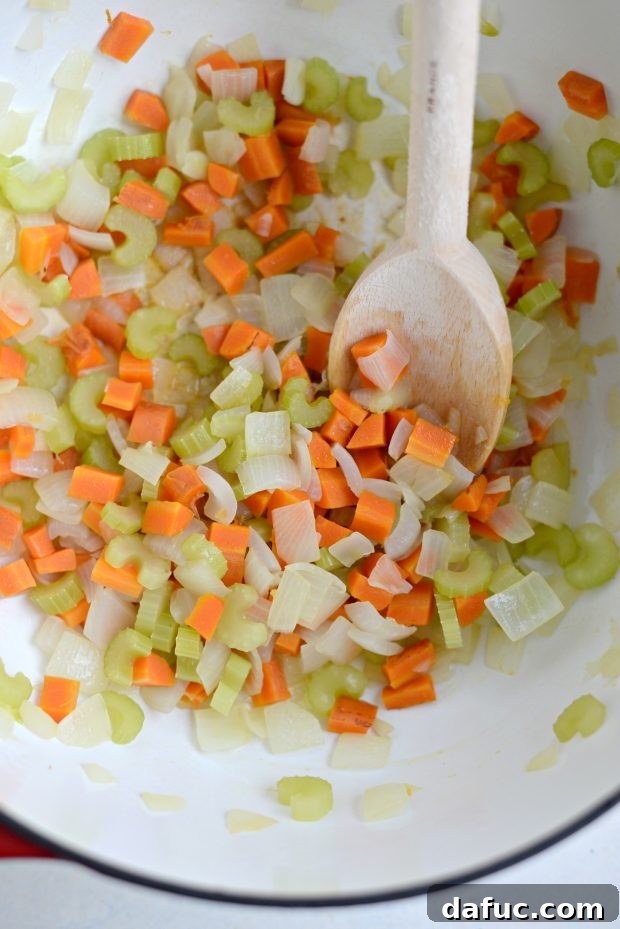 Diced carrots, onions, and sliced celery sautéing in olive oil in a Dutch oven.