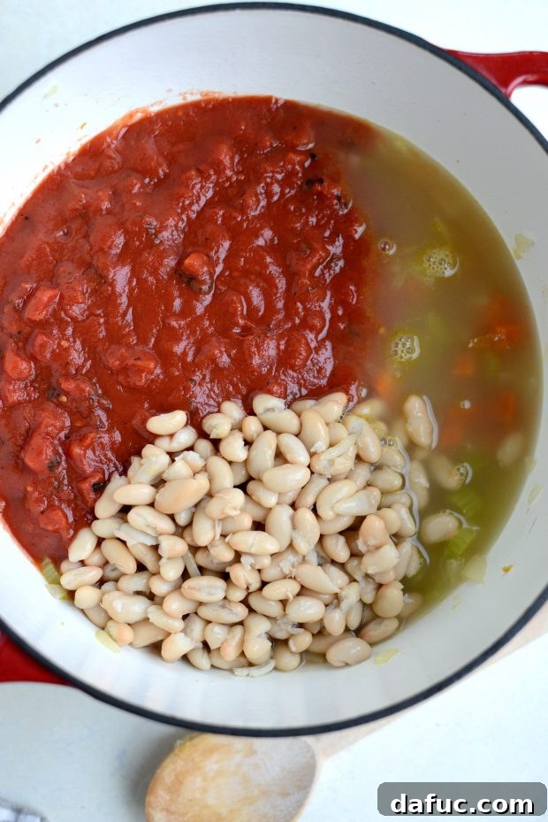 Crushed tomatoes, cannellini beans, and chicken broth being added to sautéed vegetables in a Dutch oven.